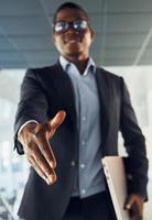 Handshake gesture. Young african american businessman in black suit is indoors photo