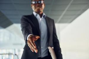 Handshake gesture. Young african american businessman in black suit is indoors photo