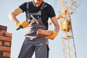 sosteniendo ladrillo y usando un martillo. trabajador de la construcción en uniforme y equipo de seguridad tiene trabajo en la construcción foto