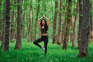 Positive brunette doing fitness outdoors in the forest at daytime photo