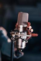 Close up view of microphone. Young beautiful female performer rehearsing in a recording studio photo