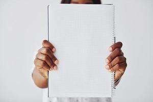 Young african american woman in formal clothes standing with notepad and empty paper in hands indoors photo