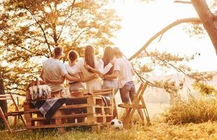 abrazándose y mirando el atardecer. grupo de jóvenes tiene vacaciones al aire libre en el bosque. concepción de fin de semana y amistad foto