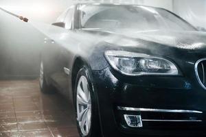 High pressured water. Modern black automobile get cleaned inside of car wash station photo