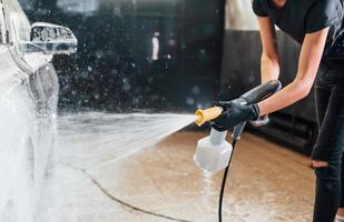 Using high pressure water. Modern black automobile get cleaned by woman inside of car wash station photo