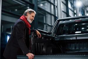 anciano de moda con cabello gris y bigote buscando un auto nuevo en el interior del salón foto