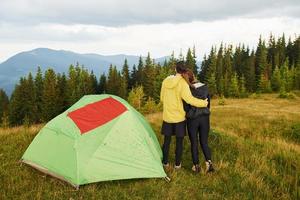 pareja abrazándose cerca de la tienda con bandera roja. majestuosas montañas de los cárpatos. hermoso paisaje de naturaleza virgen foto