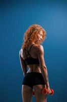 Doing warm up exercises. Redhead female bodybuilder is in the studio on blue background photo