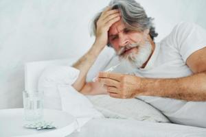 Feels sick. On the bed. Senior stylish modern man with grey hair and beard indoors photo