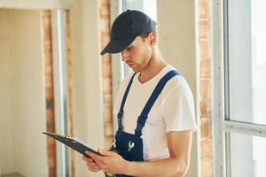 In hard hat. Young man working in uniform at construction at daytime photo