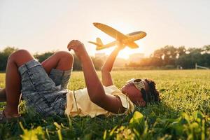 In glasses with toy plane. African american kid have fun in the field at summer daytime photo