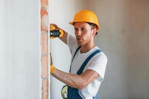 Empty walls. Young man working in uniform at construction at daytime photo