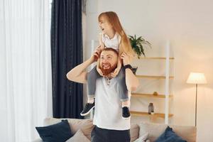 niña sentada sobre los hombros. padre con su pequeña hija está en casa juntos foto