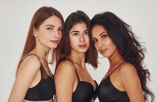 In black bra. Three young women in lingerie together indoors. White background photo