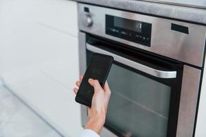 la mujer joven está adentro en la habitación de la casa inteligente controlando el horno foto