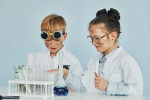 Girl with boy working together. Children in white coats plays a scientists in lab by using equipment photo