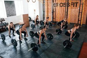 sentadillas con barra. grupo de jóvenes deportistas tienen un día de crossfit en el interior del gimnasio foto