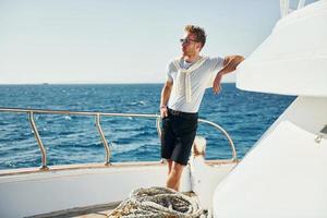 Warm weather. Young male tourist is on the yacht on the sea. Conception of vacation photo