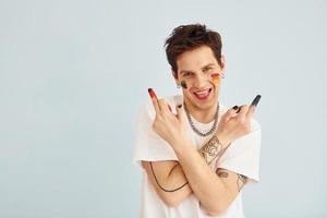 Young gay man is standing in the studio and posing for a camera. Shows middle fingers photo