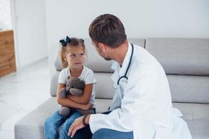 médico masculino con uniforme blanco se sienta en la clínica con una niña foto