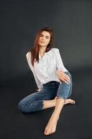 Sits on the floor. Young beautiful woman is posing for the camera in the studio photo