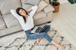 With laptop. Beautiful young woman in jeans and white shirt is at home photo