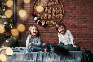 mirando a un lado y sonriendo. niñas divirtiéndose en la cama con interiores de vacaciones al fondo foto