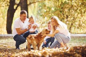 Cheerful young family with dog have a rest in an autumn park together photo