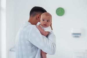 Stands and holds baby on the hands. Young pediatrician is in the clinic at daytime photo