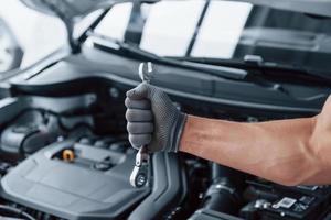 Ready for the work. Man's hand in glove holds wrench in front of broken automobile photo