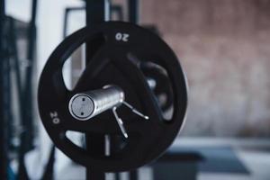 Focused on the silver colored part of barbell. Black barbell on the metal stand in the gym at daytime. No people around photo