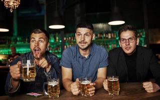 tres aficionados al deporte en un bar viendo fútbol. con cerveza en las manos foto