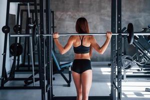 Young fitness woman with slim type of body doing exercises by using barbell photo