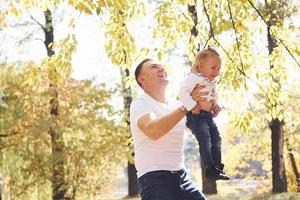 Dad holds his daughter in hands and have fun in the autumn park photo