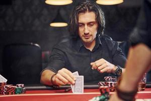 Elegant young people sits by table and playing poker in casino with smoke in the air photo