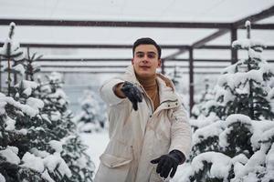 Cheerful young guy throwing snowballs outdoors near fir trees photo