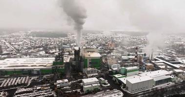 vlucht in de buurt pijpen met wit rook van houtbewerking onderneming fabriek zagerij. lucht verontreiniging concept Aan industrieel landschap in winter met sneeuw video