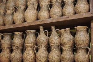 Many handmade clay jugs on shelf in workshop photo