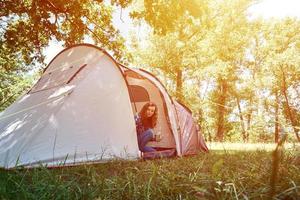 Woman looking out of tourist tent on sunny morning in the forest photo