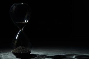 reloj de arena sobre fondo oscuro, primer plano. concepto de urgencia y agotamiento del tiempo foto