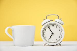 White retro alarm clock and cup on yellow background. Morning time concept photo