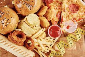 Different types of fastfood and snacks on the table with measuring tape photo