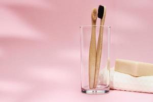 cepillos de dientes de bambú en el cristal y sombras de hojas sobre fondo rosa foto