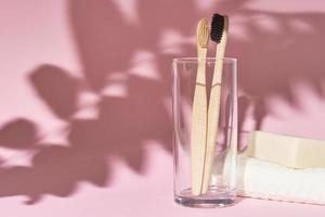 cepillos de dientes de bambú en el cristal y sombras de hojas sobre fondo rosa foto