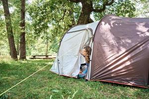 Woman looking out of tourist tent on sunny morning in the forest photo