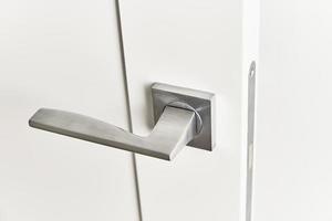 Silver door handle on a white door.  Furniture accesories, interior element photo
