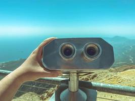 una plataforma de observación con binoculares con grandes lentes negros contra el cielo. lupa de ambiente. binoculares panorámicos para turistas, un hombre lo sostiene con la mano foto