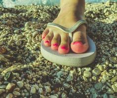 una niña con dedos grandes y una pedicura rosa en los pies camina en un país cálido con zapatillas de goma blanca. zapatos de ocio se encuentra en la arena. pizarras para caminar por la costa del mar foto