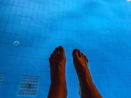 vacaciones en el mar en la playa. turista tomando el sol en una tumbona junto a la piscina. piernas masculinas blancas. piscina con agua turquesa, clorada, en el fondo de la rejilla para purificación de agua foto