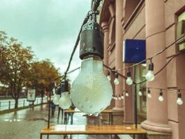 decorative light bulb hanging on a wire in the yard. cozy and cute patio, lamps in drops of water, rain outside. beauty in the courtyard of a residential area photo